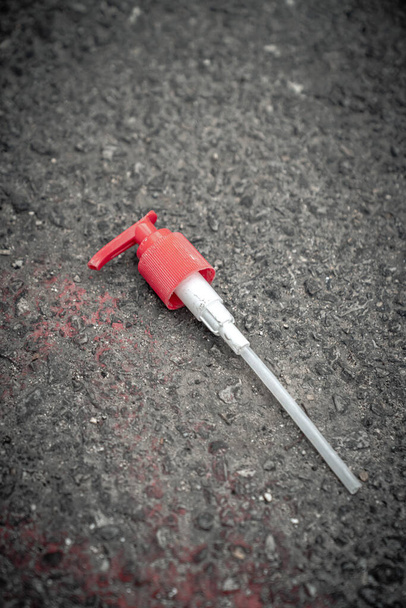 Widok z bliska czerwonej pompy z tworzywa sztucznego bez pojemnika z przezroczystą plastikową słomką zaśmiecającą czarny asfalt w alejce podczas COVID-19 lub blokady wirusa korony w Chicago - Zdjęcie, obraz