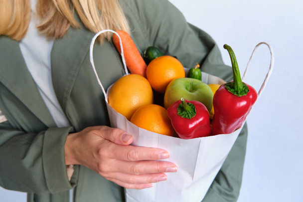 Woman in trench coat with a pack of natural fresh vegetables and fruits. Healthy eating, bio organic food. Shopping at the grocery store. Female diet. Vegetarian lifestyle. Product set for cooking - Photo, image