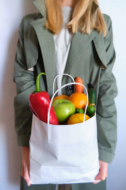 Woman in trench coat with a pack of natural fresh vegetables and fruits. Healthy eating, bio organic food. Shopping at the grocery store. Female diet. Vegetarian lifestyle. Product set for cooking - Фото, зображення