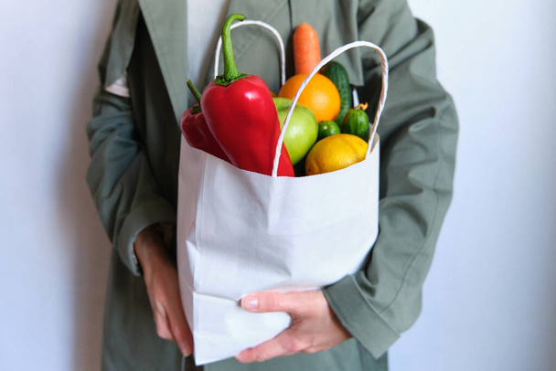 Woman in trench coat with a pack of natural fresh vegetables and fruits. Healthy eating, bio organic food. Shopping at the grocery store. Female diet. Vegetarian lifestyle. Product set for cooking - 写真・画像