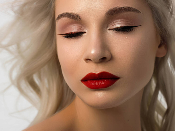 Close-up beauty of a female face with fashion evening make-up. Black liner on the eyes and extremely long eyelashes, on full lips matte scarlet lip color. Well-groomed skin after spa. red lipstick - Fotó, kép