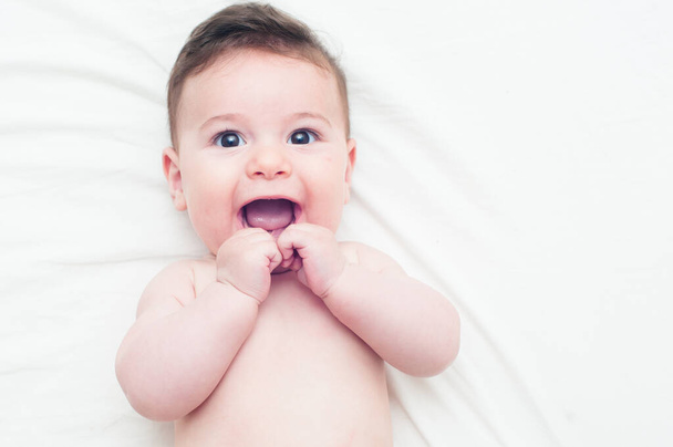 cute baby lying in bed looking at the camera with his hands on his mouth - Photo, Image