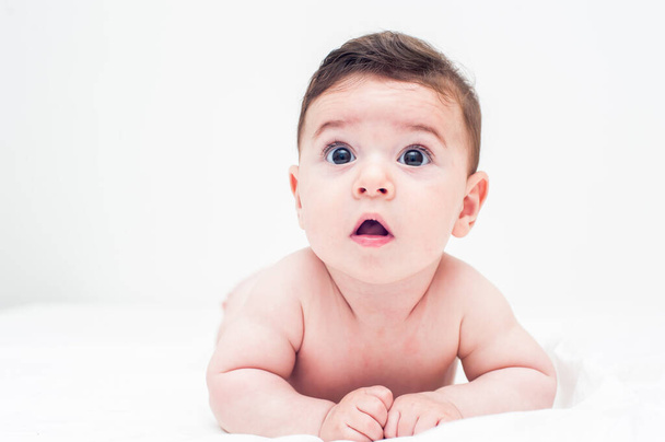 cute baby lying on his stomach in bed on a white background. Image with great copy space. - Photo, Image
