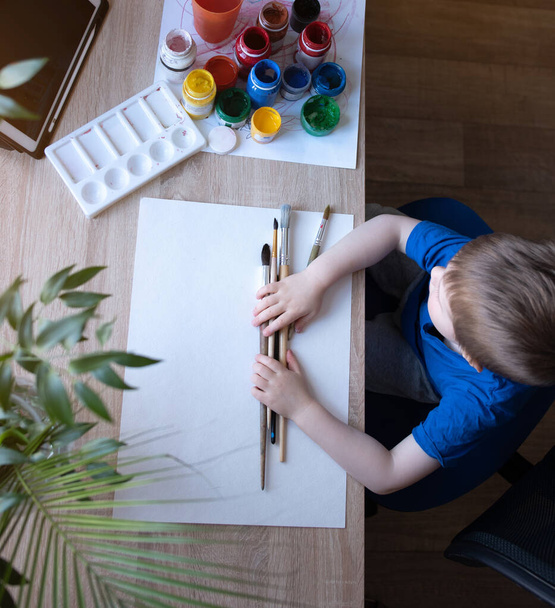 A little boy learns to draw from an online lesson. Drawing with paints at home. - Foto, imagen