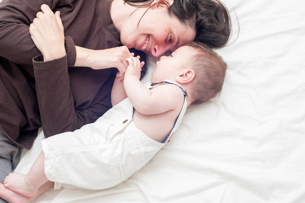 Todellinen onnellinen äiti pehmeästi pitää hänen vauva sängyssä
 - Valokuva, kuva