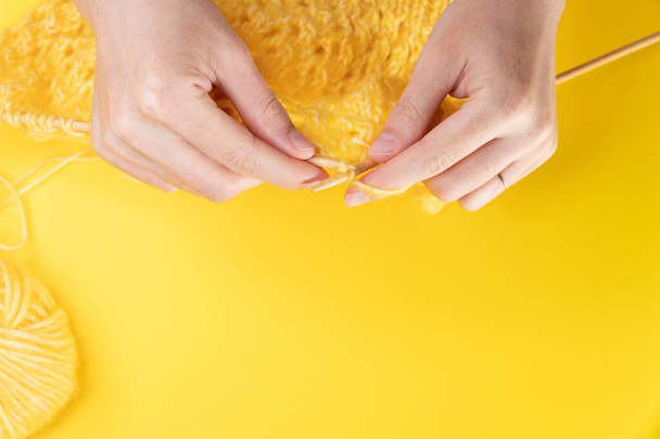 Women's hands knit from yellow wool on a yellow background, top view. Hand knitting - 写真・画像