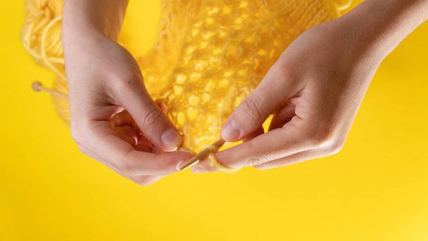 Women's hands knit from yellow wool on a yellow background, top view. Hand knitting - Foto, Imagen