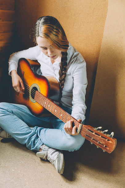 Stay Home Stay Safe. Young woman sitting in room on floor and playing guitar at home. Teen girl learning to play song and writing music. Hobby lifestyle relax Instrument leisure education concept - Photo, image