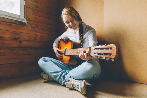 Залишайтеся вдома в безпеці. Молода жінка сидить у кімнаті на підлозі і грає на гітарі вдома. Дівчинка вчиться грати в пісню і писати музику. Хобі спосіб життя розслабтеся Інструмент дозвілля Освіта концепція
 - Фото, зображення
