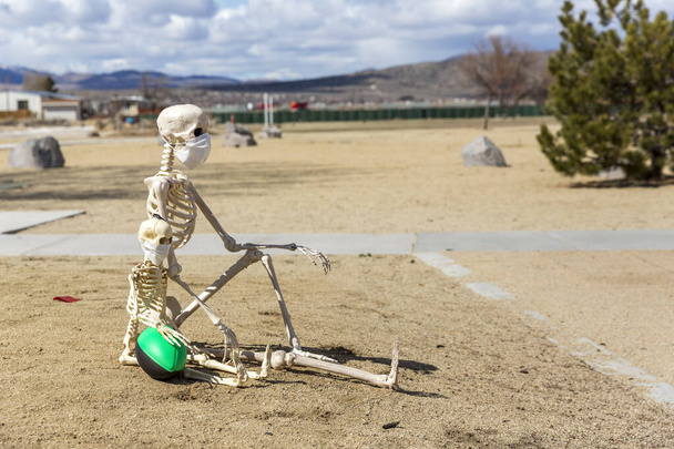 esqueletos de adultos y niños sentados mirando a un parque cerrado vacío en un buen día
 - Foto, Imagen