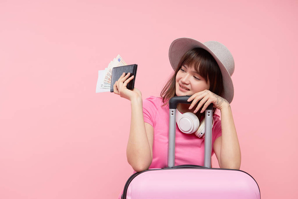 Joven turista asiática con pasaporte, pasajes de avión y maleta rosa sobre fondo rosa. El concepto de en los aeropuertos y el cierre de las fronteras internacionales para viajar a cuarentena
 - Foto, imagen
