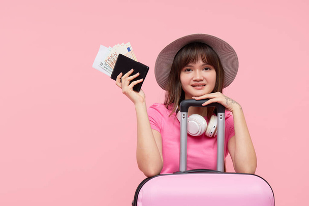Pasaportu, uçak biletleri ve pembe arka planda pembe valizi olan genç Asyalı kadın turist. Havaalanlarında karantinaya gitmek için uluslararası sınırları kapatma kavramı - Fotoğraf, Görsel