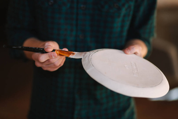 Закрыть руки гончаров, делающих орнамент на керамической продукции. Тарелка в руках у мужчин. Молодой художник
 - Фото, изображение