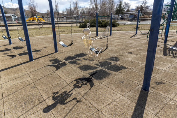 Esqueleto balançando no brinquedo das crianças em um parque fechado vazio em um bom dia
 - Foto, Imagem