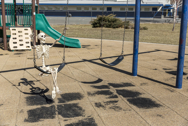 Скелет гойдається на дитячій іграшці в порожньому закритому парку в гарний день
 - Фото, зображення