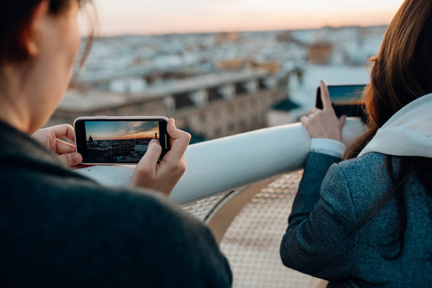 Young woman taking pictures with smart phone,enjoying sunset from a cityscape viewpoint.Tourist having amazing experience in Seville,Andalucia,Spain.Enjoying sunshine and panorama.Travel photography - 写真・画像