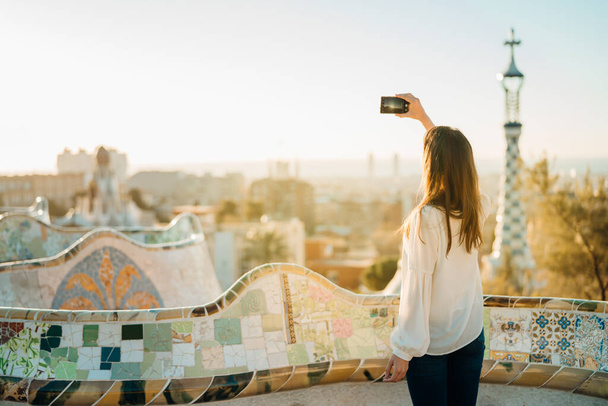 Female travel photographer/videographer and bloger using advanced new phone camera with internal stabilisation in Barcelona,Spain.Travel photography/cinematography,vlogger visiting Parc Guell. - Foto, imagen