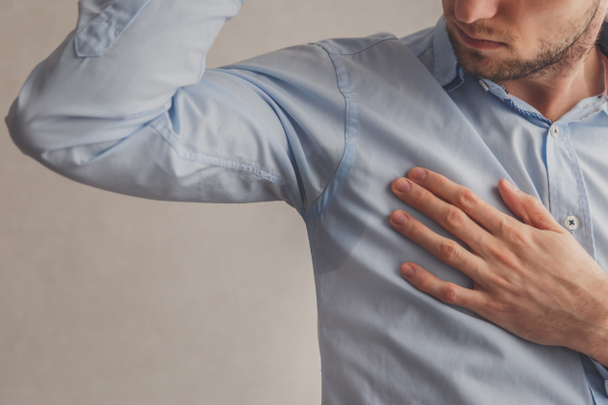 Hombre con hiperhidrosis sudando muy mal bajo la axila en camisa azul, en gris
 - Foto, Imagen