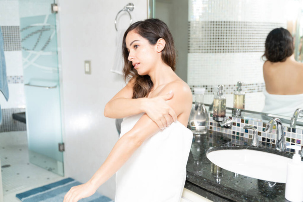 Žena zabalená v ručníku v koupelně a dávat na nějaké tělo hydratační krém na její tělo - Fotografie, Obrázek