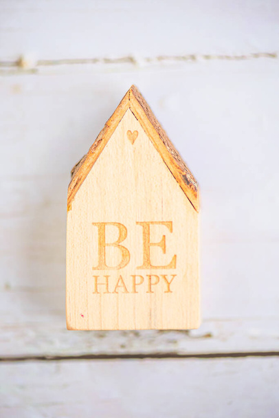 επιγραφή "να είναι ευτυχισμένος" σε ένα κομμάτι ξύλο σε σχήμα σπιτιού - Φωτογραφία, εικόνα