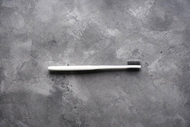 Плоская композиция белой зубной щетки с черными щетинами на сером фоне
 - Фото, изображение