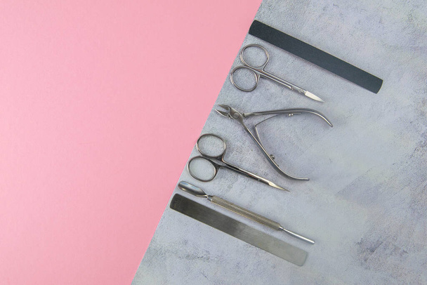 Um conjunto de ferramentas cosméticas para manicure e pedicure. Tesoura de manicure, cutículas, serras, moleiro e toalha em um fundo rosa de concreto. Principais vistas com espaço livre
 - Foto, Imagem