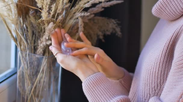A nő kezében Yoni tojás készült átlátszó lila ametiszt kő tüskék háttér áll az ablak közelében beltérben. Női egészség koncepció, vumfit, imbuilding vagy meditáció - Felvétel, videó