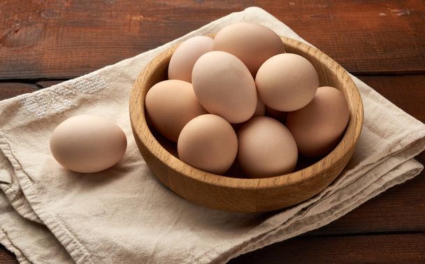 сирі коричневі домашні курячі яйця в дерев'яній тарілці на столі, вид зверху
 - Фото, зображення