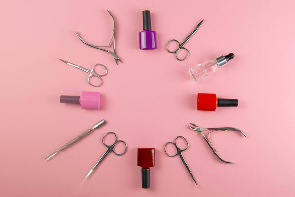 Un conjunto de herramientas cosméticas para la manicura y la pedicura sobre un fondo rosado. Esmaltes de gel dispuestos en forma de círculo y tijeras de manicura vista superior con espacio libre
 - Foto, Imagen