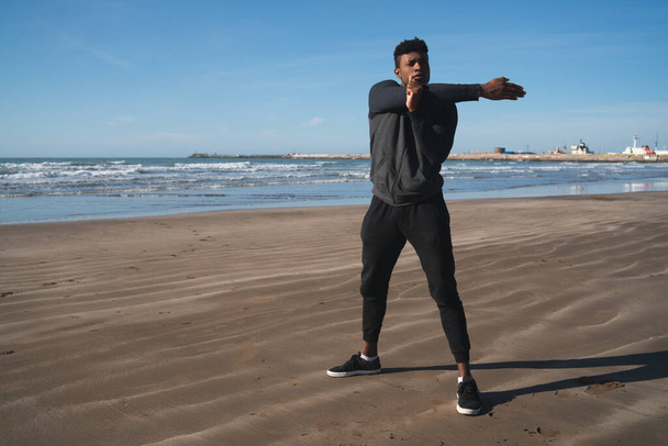 Portrait of an athletic man stretching arms before exercise at the beach. Sport and healthy lifestyle. - Φωτογραφία, εικόνα