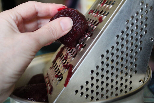 on a metal grater, put red beets / photo metal grater for vegetables. RUB your hand on a grater red beets in a plate. food for lunch, dinner, and Breakfast. - Photo, Image