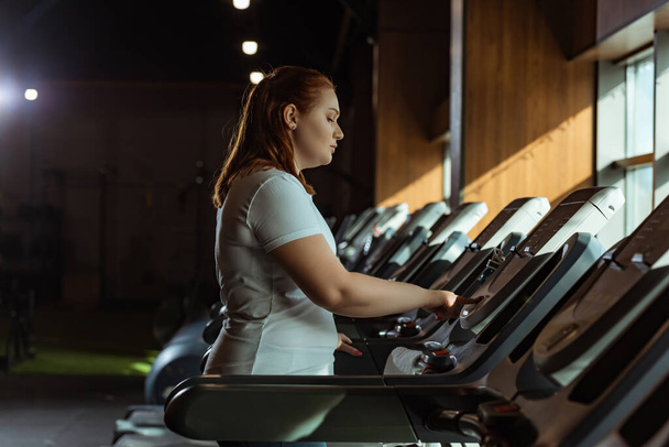 side view of focused overweight girl training on treadmill in gym - Fotó, kép