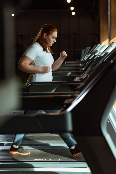 selective focus of focused overweight girl running on treadmill in gym - Foto, Bild