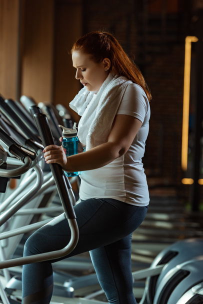 unavená dívka s nadváhou drží sportovní láhev při tréninku na stepper - Fotografie, Obrázek