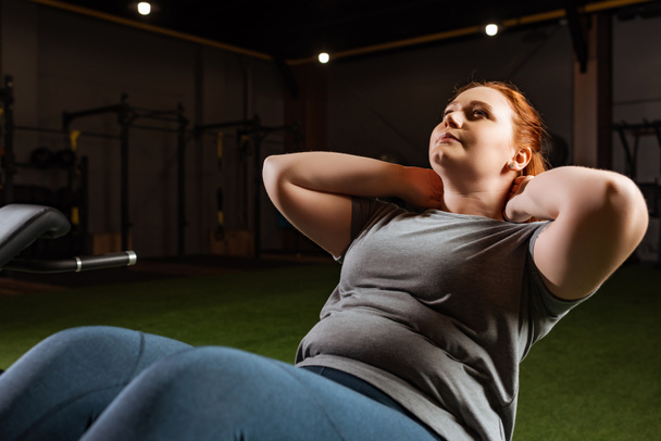pretty, overweight girl doing abs with hands behind head in gym - Photo, Image