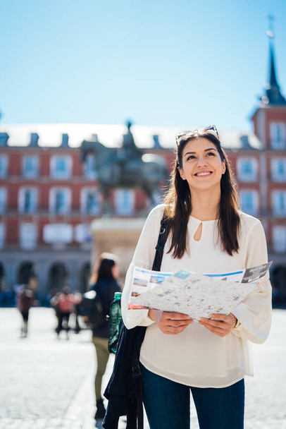Young happy woman exploring center  of Madrid. visiting famous landmarks and places.Cheerful female traveler at famous Plaza Mayor square admiring statue of Philip III.Spain travel experience. - Foto, Imagem