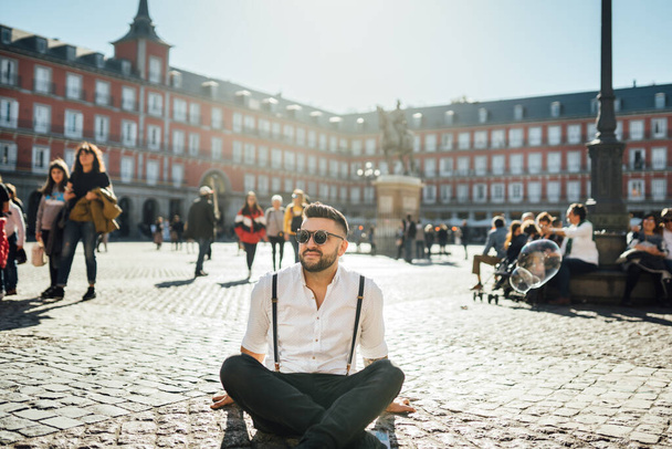 Attractive young man influencer.Tourist visiting famous landmarks and places.Cheerful male traveler at famous Plaza Mayor square, site seeing attractions.Vacation in Spain, blogger lifestyle - Фото, изображение