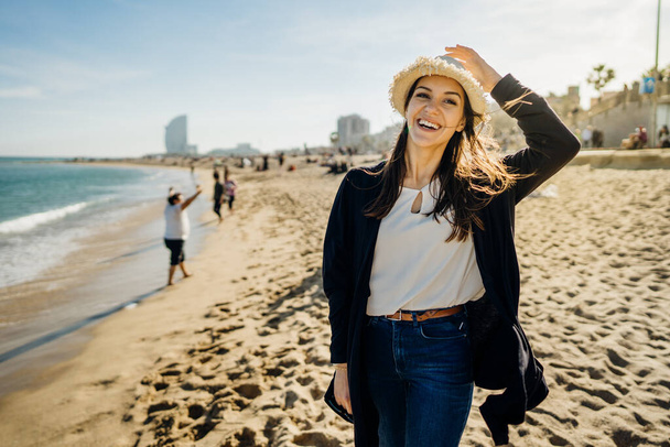 Gondtalan nő turista élvezi a strandon.Vidám nő szalmakalapos séta a homokos strandon tavasszal a szél fúj vályú a haját.Női utazó Barceloneta strand Barcelonában, Spanyolország - Fotó, kép