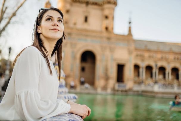 Enjoying beautiful historical landmark.Young tourist woman looking over Plaza de Espana in Seville,Andalusia,Spain.Traveling to Spain.Sunset on Spain Square.Pensive woman in public square in Europe. - Фото, изображение