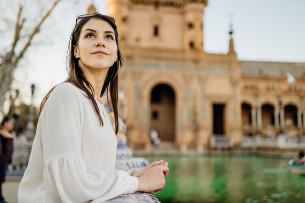 Enjoying beautiful historical landmark.Young tourist woman looking over Plaza de Espana in Seville,Andalusia,Spain.Traveling to Spain.Sunset on Spain Square.Pensive woman in public square in Europe. - Zdjęcie, obraz