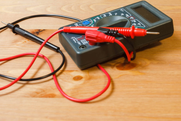電流と電圧を測定するためのマルチメータ。木製の背景に様々な電源でボルトとアンプを測定およびテストするための電極とワイヤを備えたマルチメータ - 写真・画像