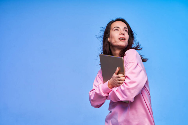 Young exited woman holding tablet in both hands dressed in pink on blue background - Foto, Bild