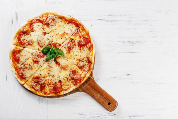 Hot true PEPPERONI ITALIAN PIZZA with salami and cheese. TOP VIEW Tasty traditional pepperoni pizza on board on white wooden table. Copy space for your logo. Ideal for commercial  - Foto, Imagem