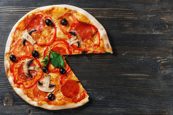 Blick von oben auf das italienische PIZZA mit Pilzen, Basilikum, Tomaten, Oliven und Käse. OHNE ein Stück. Dunkler Holztischhintergrund. Siehe Prosciutto, Capricciosa, Funghi, Cotto PIZZA. Ideal für kommerzielle Zwecke - Foto, Bild
