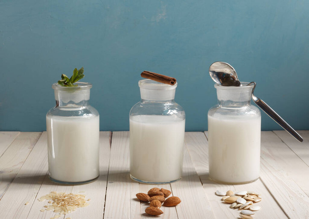 various types of plant-based lactose-free milk in glass bottles on a blue background, horizontally - Zdjęcie, obraz