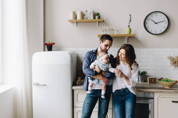 Beautiful caucasian family of three in the kitchen, mother, father and baby girl - Zdjęcie, obraz