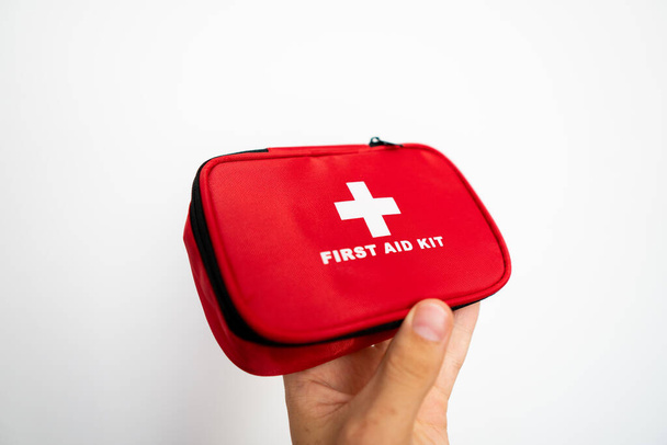 Mans hand holding a red first-aid kit with a white wall on background. - 写真・画像