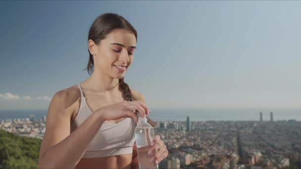 Woman opening bottle at viewpoint of city. Girl drinking water after training - Filmmaterial, Video