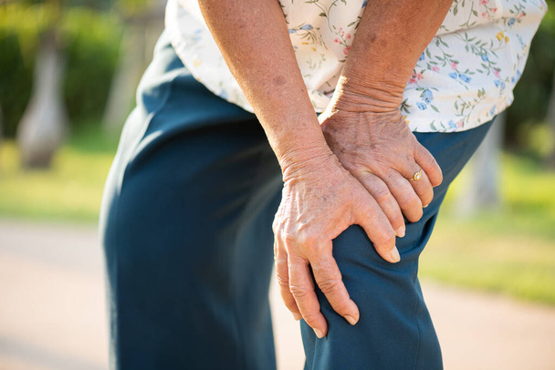 Азиатская старуха, прогуливающаяся в парке с болью в колене, травмой колена в парке. Концепция здравоохранения
. - Фото, изображение
