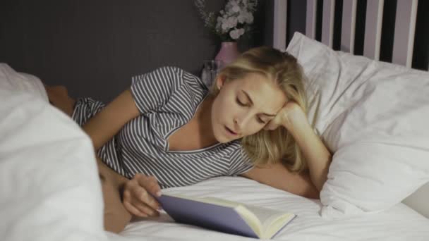Mladá dívka ležící na posteli a čtení knihy ve svém volném čase - Záběry, video